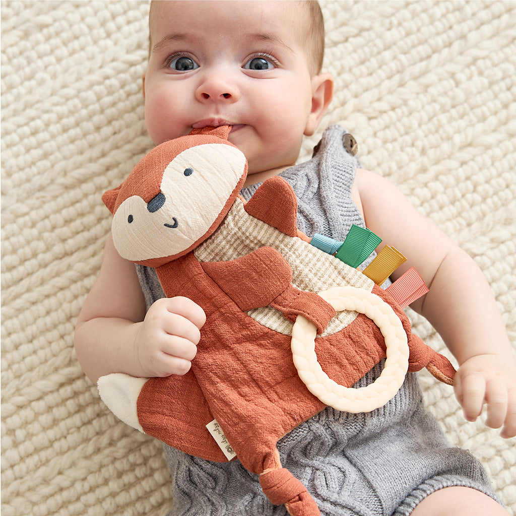 Baby holding a soft toy with a smile on a textured surface