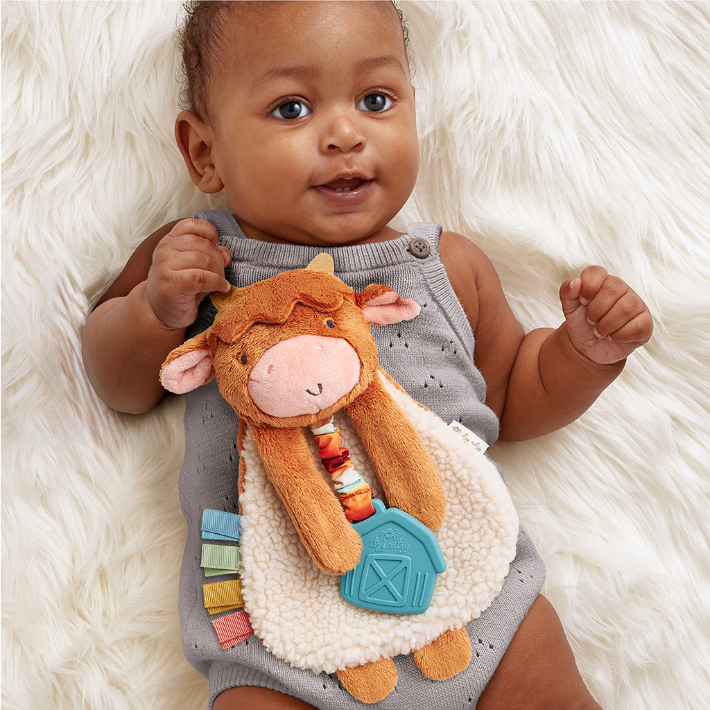 Baby lying on a fluffy white surface holding a plush cow toy.