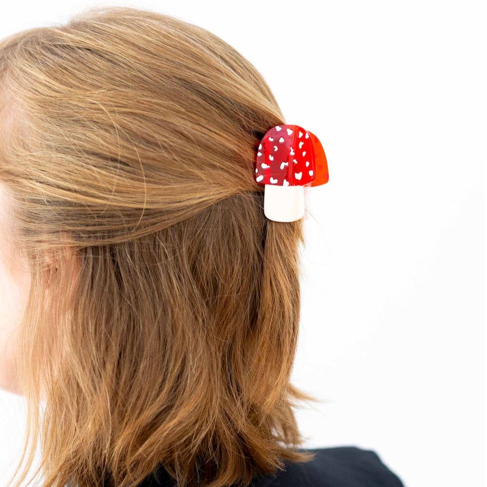 Red and white mushroom-shaped hair clip on a person's hair against a white background