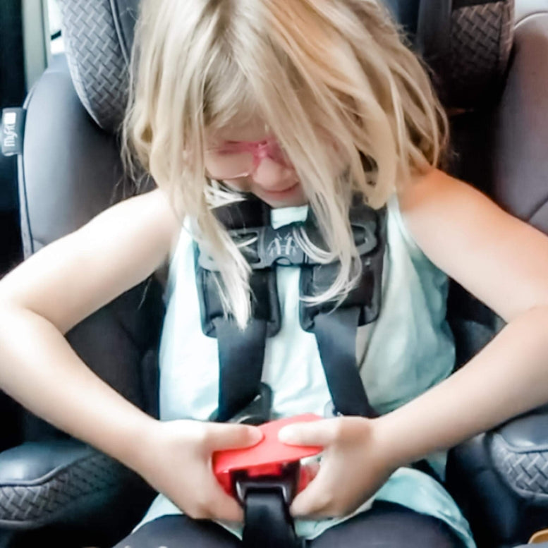 Child in a car seat with a red buckle being fastened
