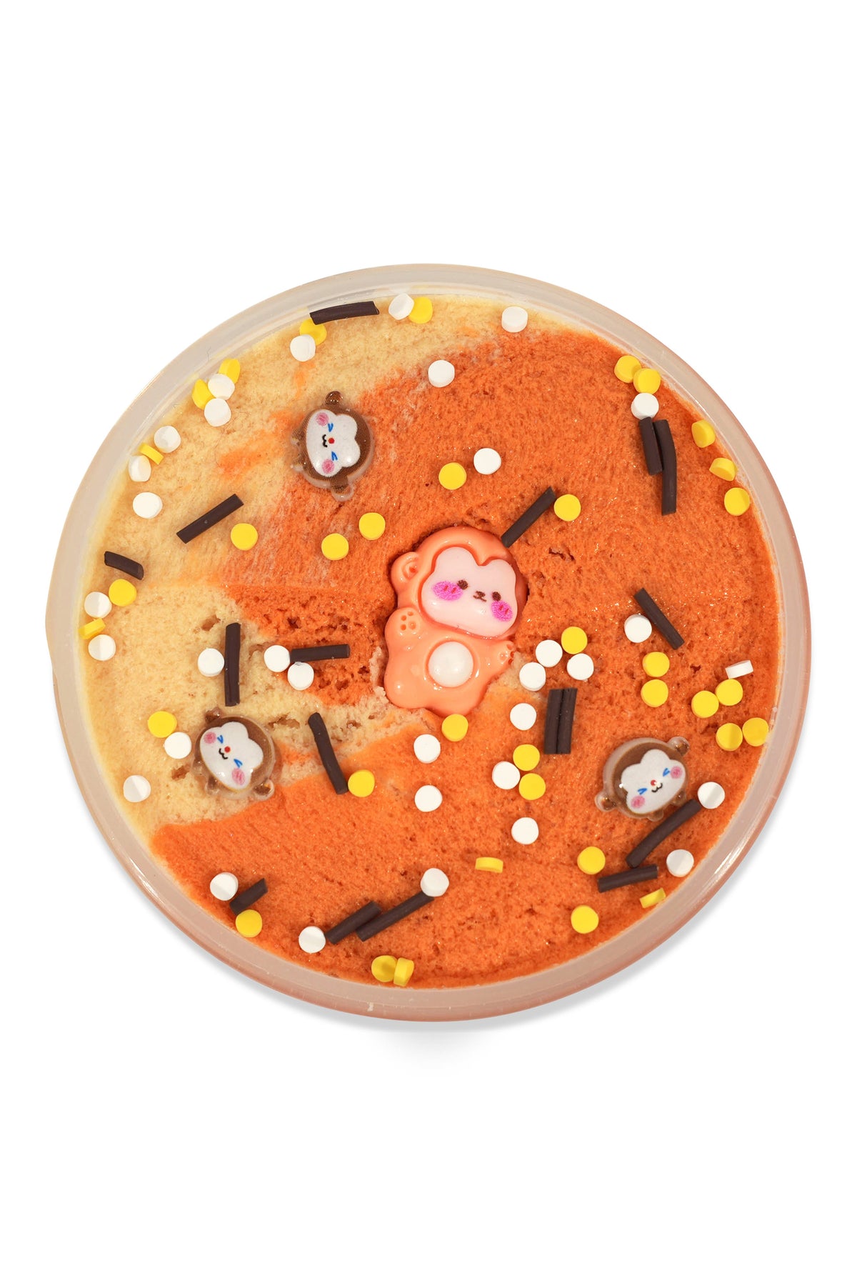 A round, shallow dish filled with orange and beige marbled slime, decorated with small white, yellow, and black sprinkles, chocolate-like pieces, and a central pink bear-shaped topper, photographed on a white background.