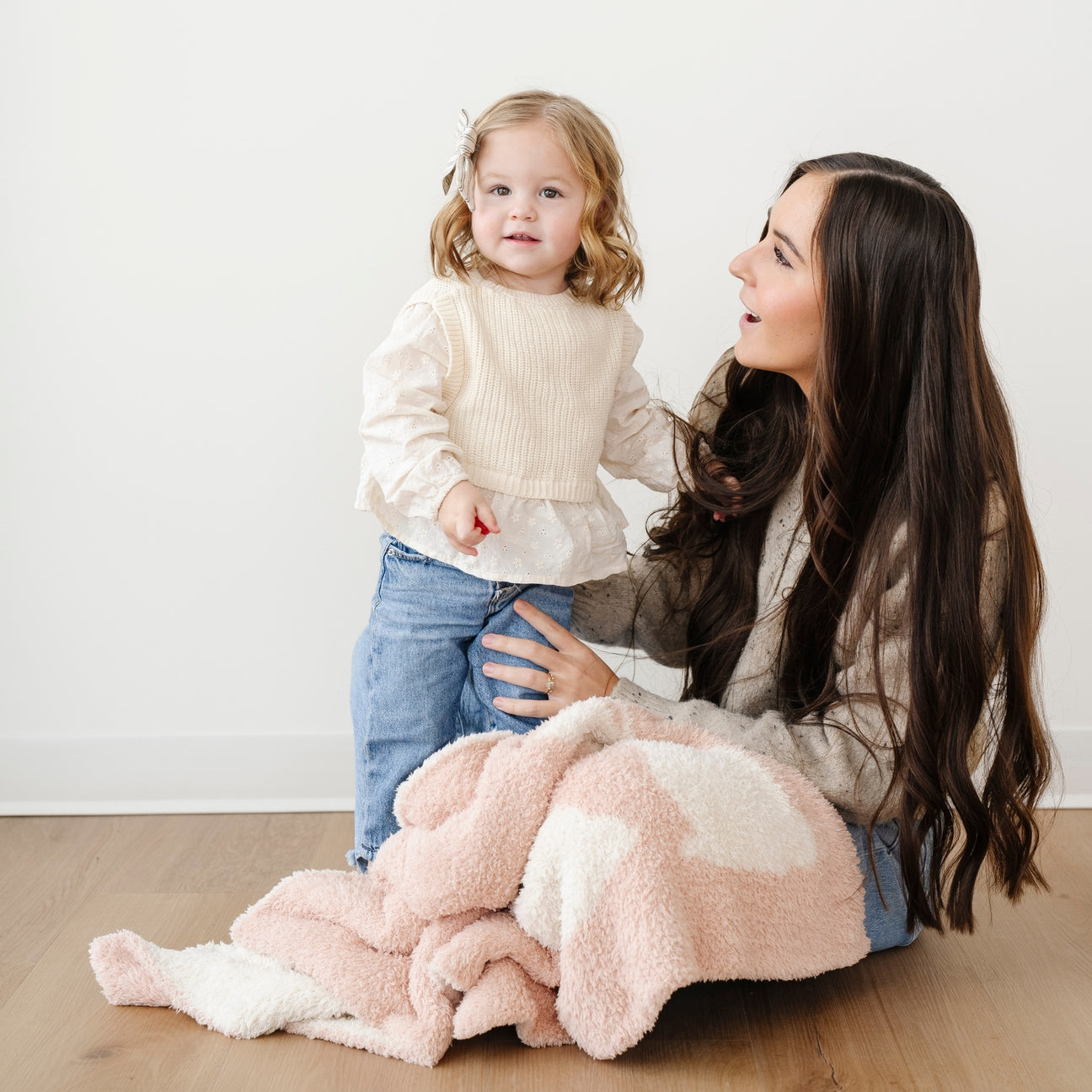 Woman and child sitting on a wooden floor with a pink and white blanket