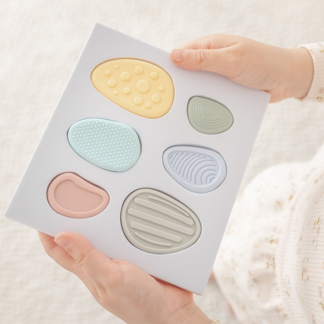 Hand holding a makeup product with pastel-colored textured stones on a light background