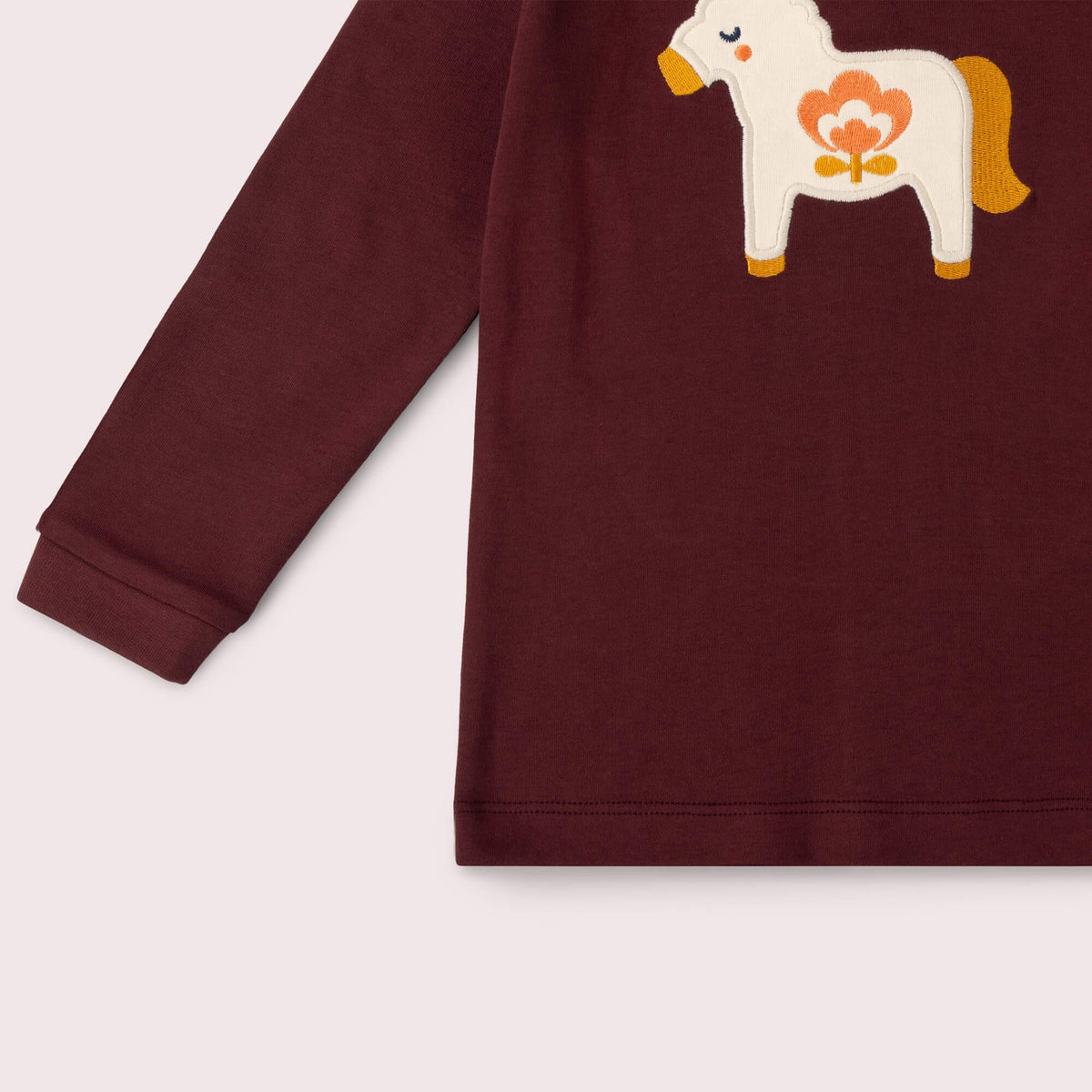 A close-up of a long-sleeve burgundy children's sweatshirt featuring a white embroidered Dala horse with orange and yellow details on the chest, set against a light beige background.