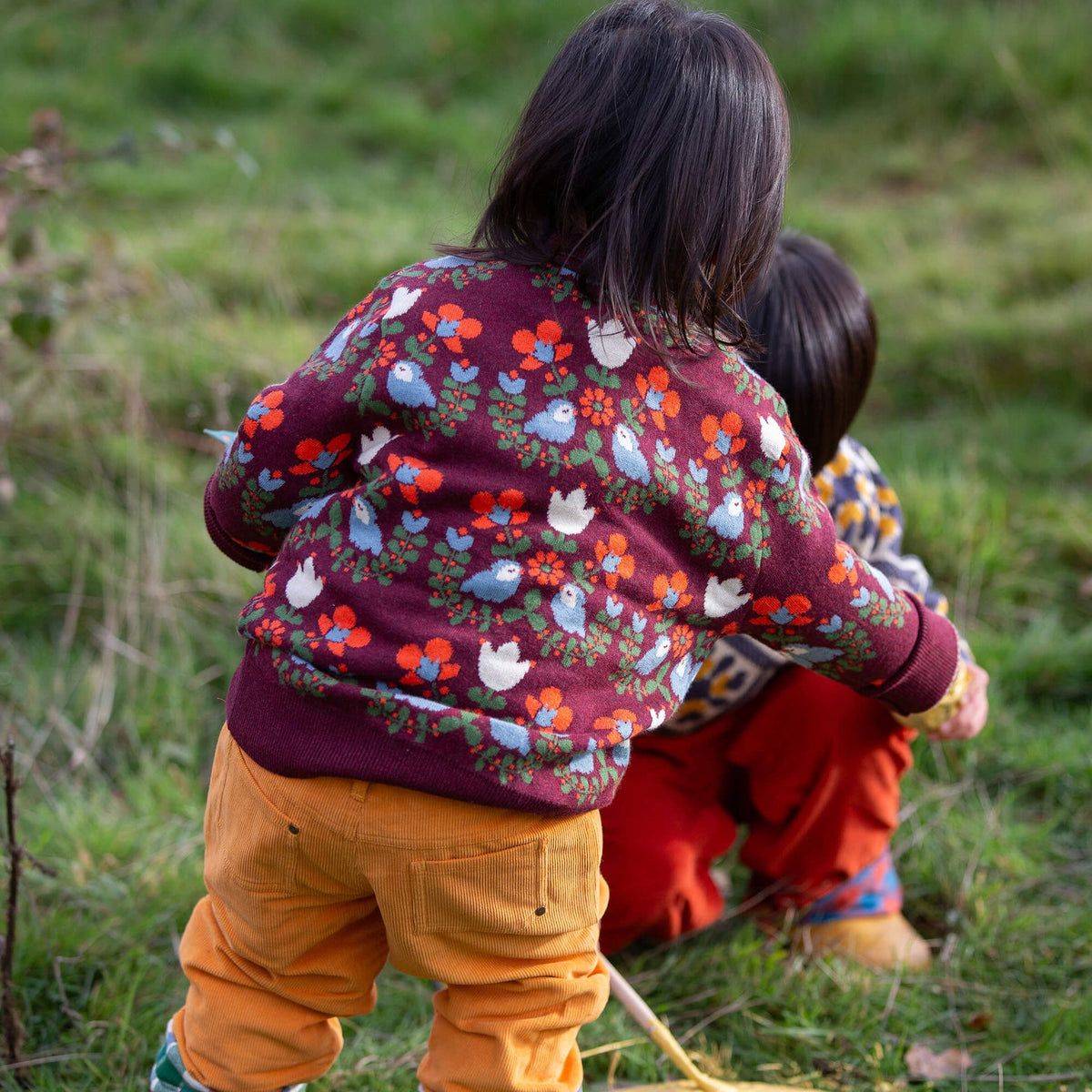 Two children wearing patterned sweaters outdoors in a natural setting