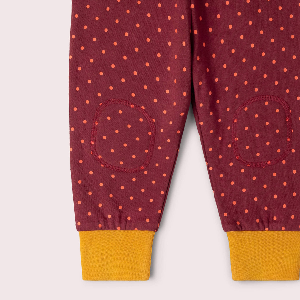 Maroon children's pants with orange polka dots and yellow cuffs on a white background