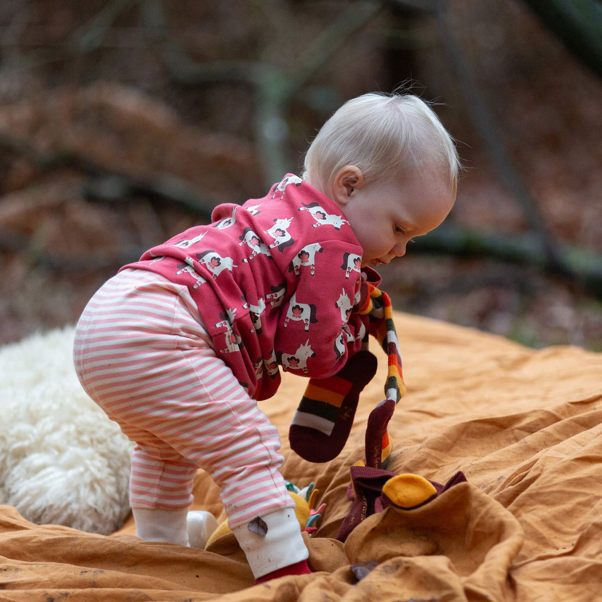 Child in pink outfit with animal patterns standing on a blanket in a forest setting