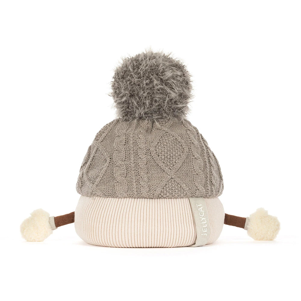 A gray cable-knit beanie hat with a fluffy gray pom-pom on top, a cream ribbed lower section, and small cream pom-poms at the ends of brown ear-like extensions. A side tag reads JELLYCAT.