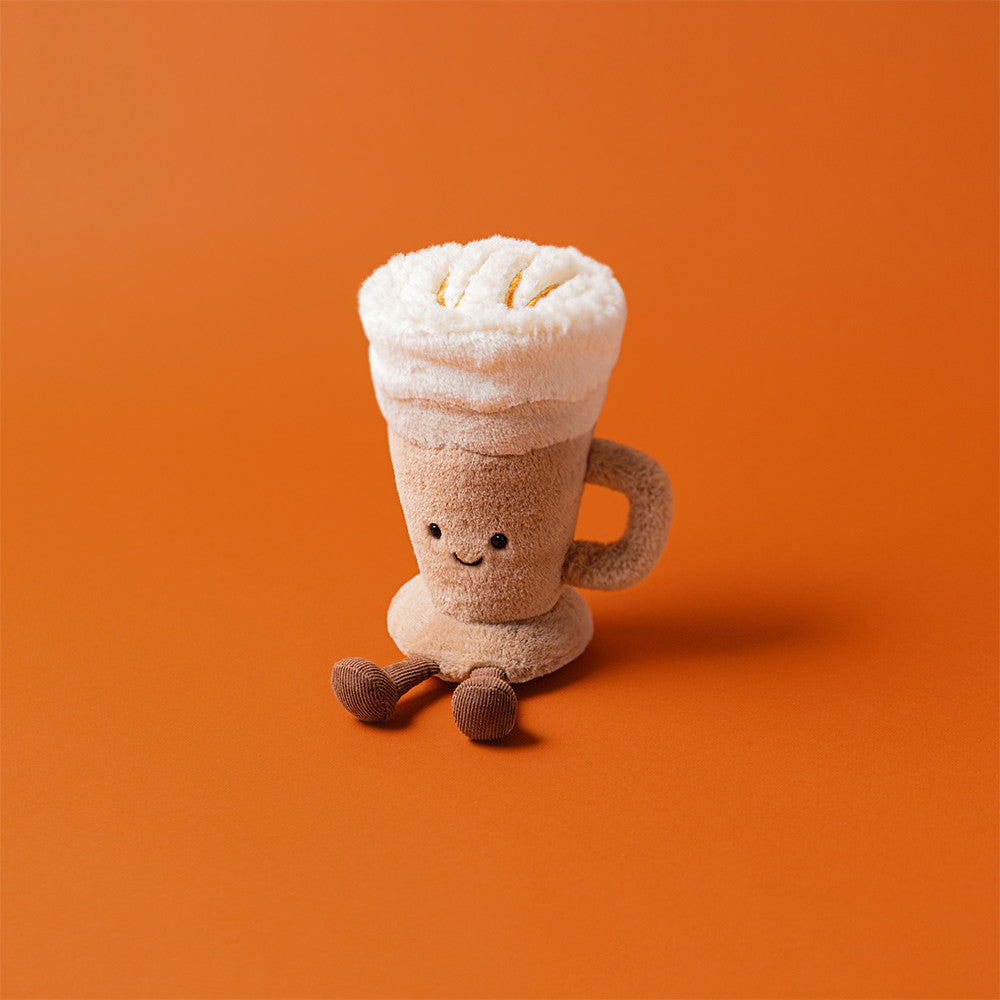 Plush toy resembling a cup of hot chocolate with whipped cream on an orange background