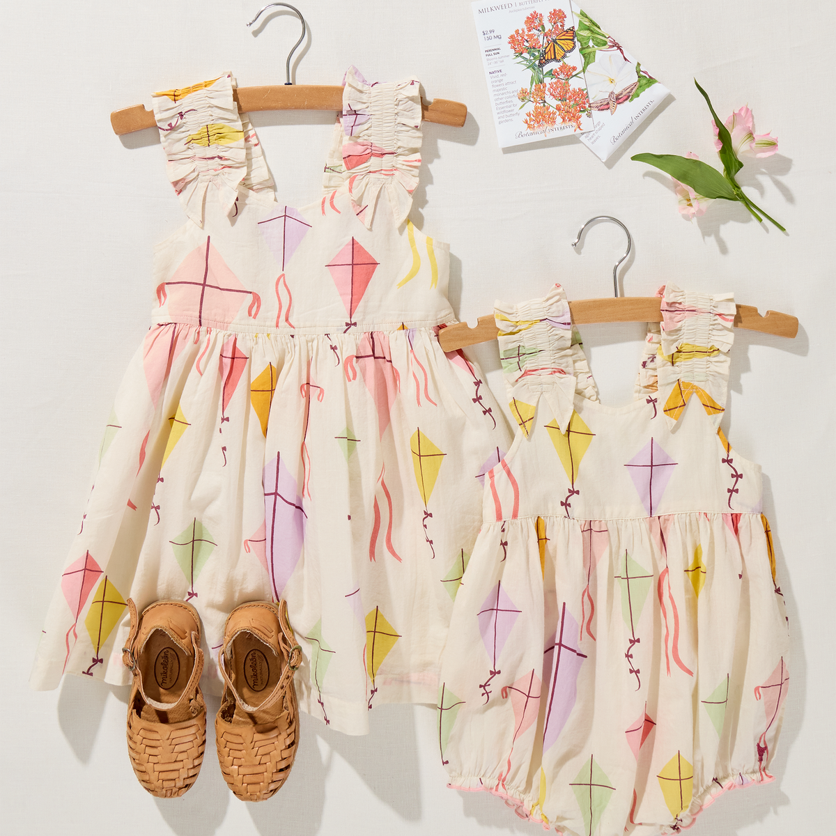 Two children's rompers with colorful patterns on hangers against a white wall.