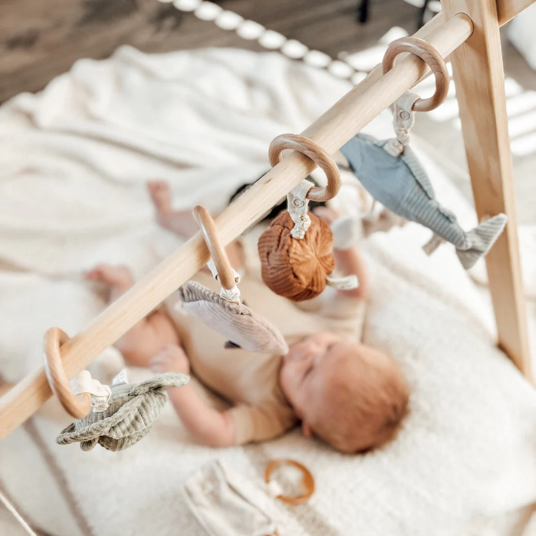 Baby lying on a blanket with a wooden play gym and hanging toys