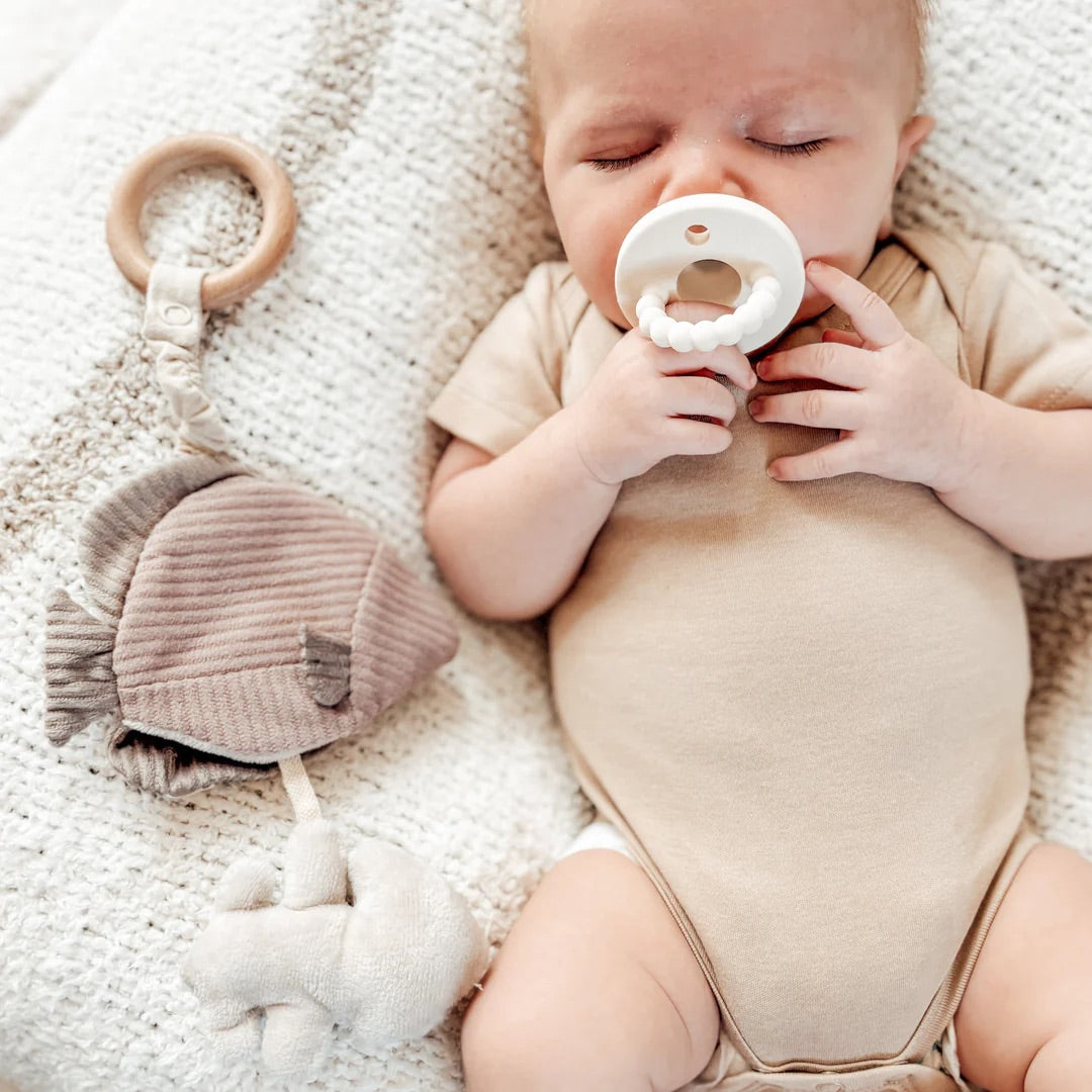 Baby lying on a soft surface with a teething ring and toy nearby