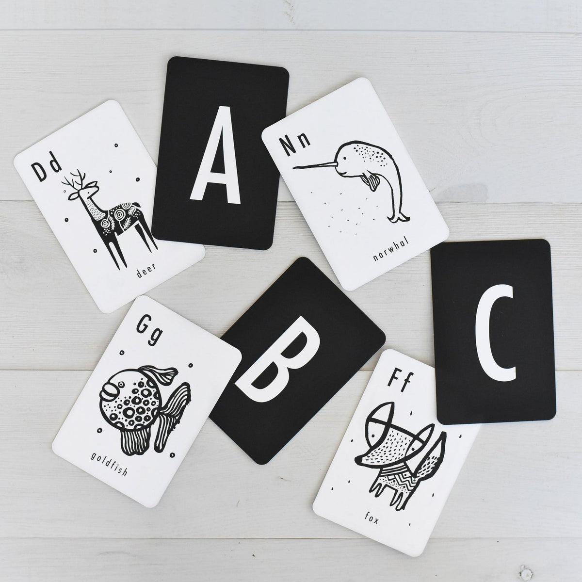 seven black and white cards showing letters and animals on a textured white wood background
