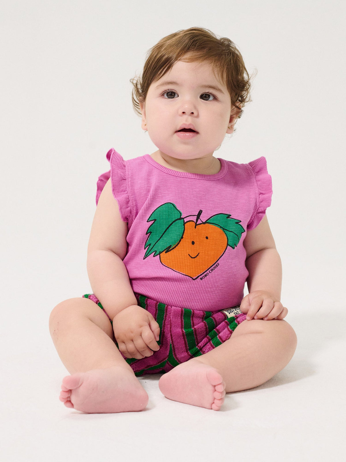 Baby wearing a pink shirt with a peach design on a white background