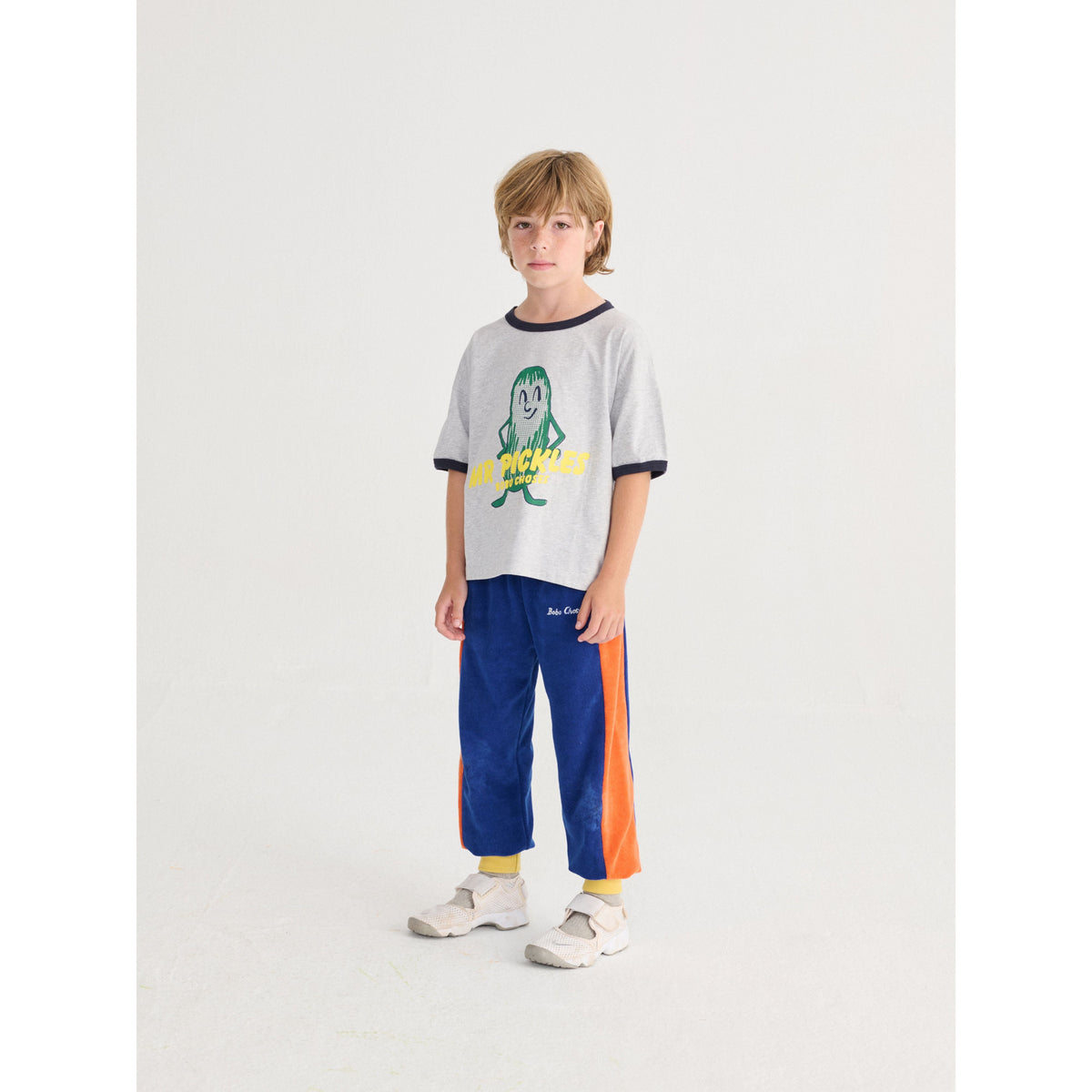 Child wearing a gray t-shirt with a graphic design and blue pants with orange accents on a white background