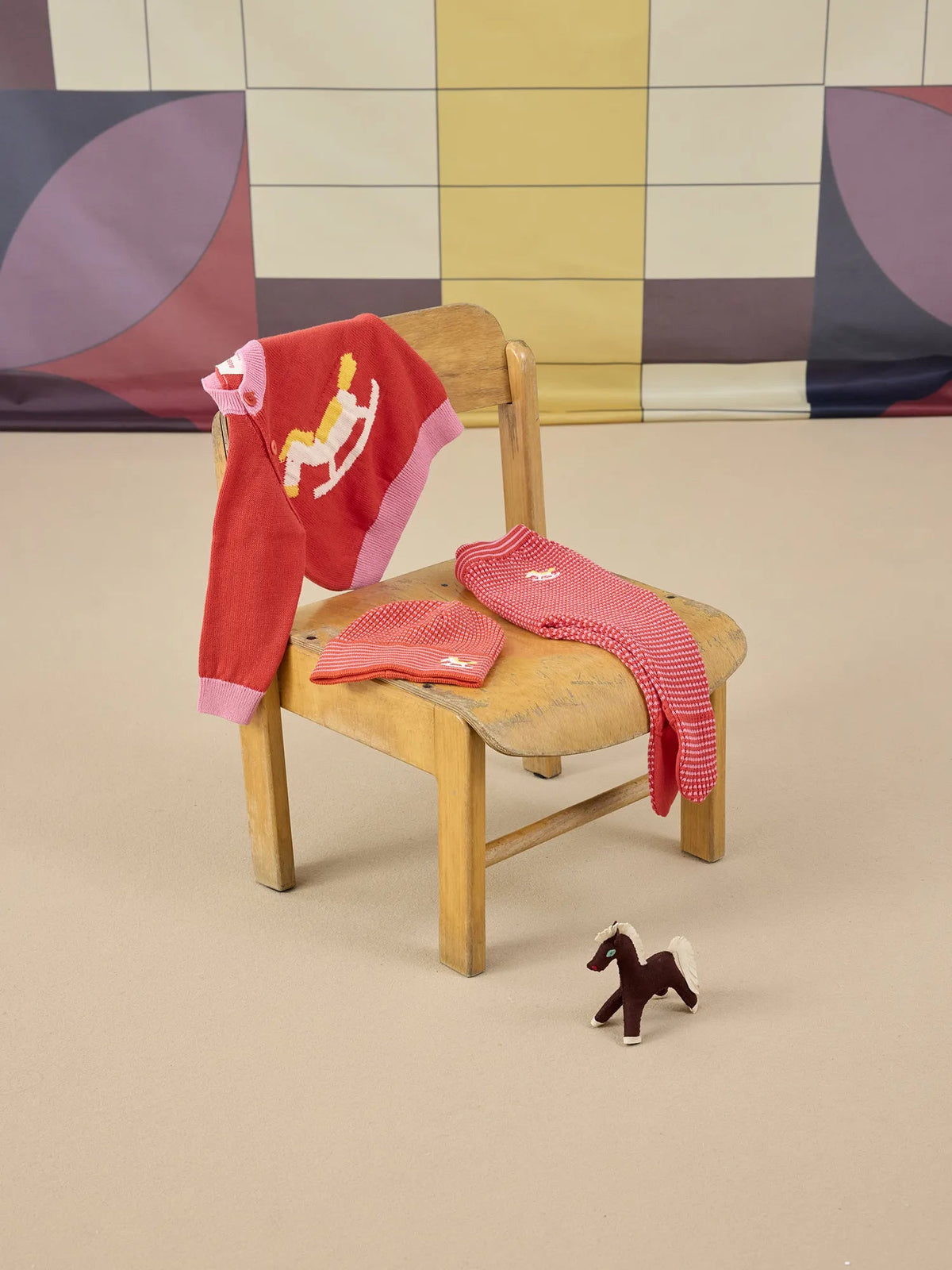 Red sweater with horse design on a wooden chair against a colorful wall.