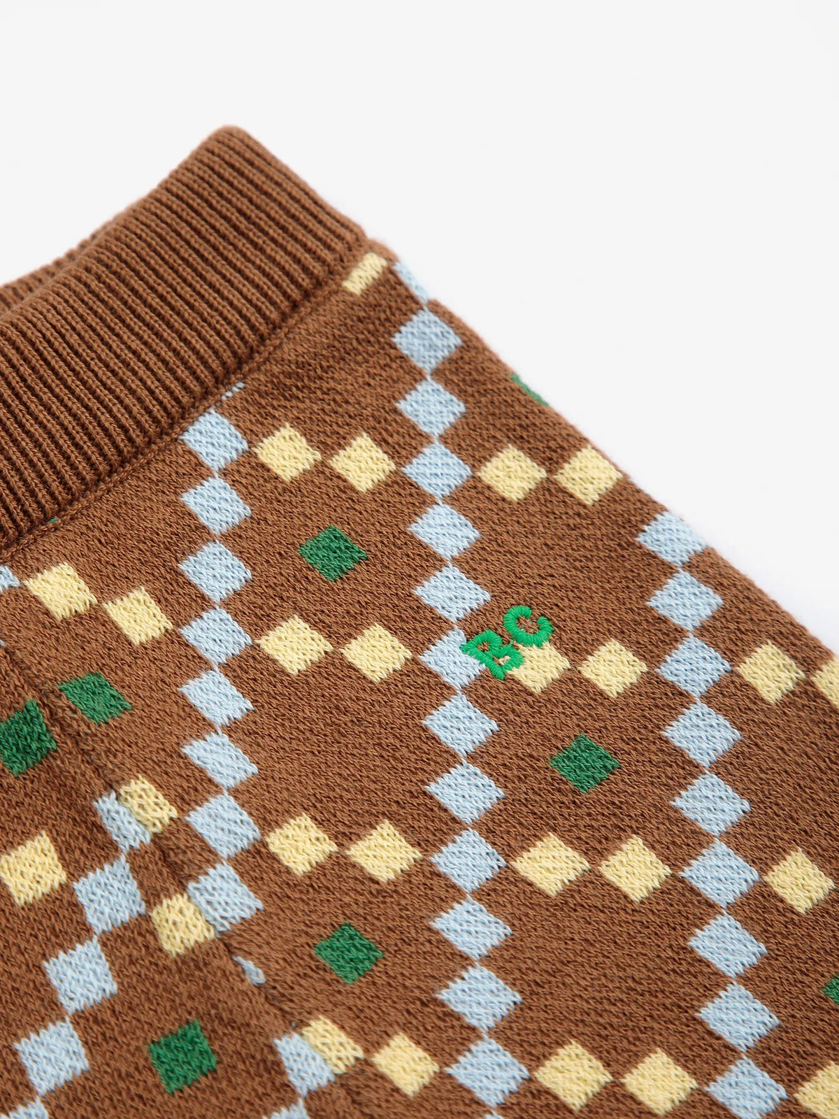 Close-up of a brown knit garment, likely a sweater or scarf, featuring a diamond argyle pattern in light blue, pale yellow, and green, with a ribbed brown collar.