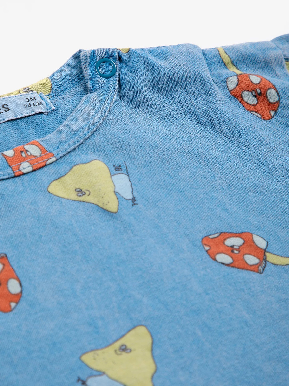 Close-up of blue fabric with cartoon mushroom patterns and a button.