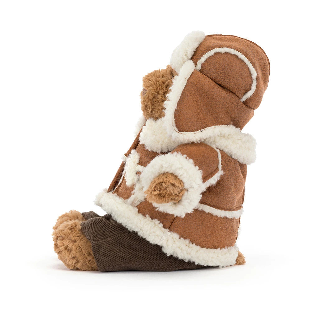 A plush teddy bear dressed in a brown suede-like winter coat with cream sherpa lining and a dark brown bootie underneath, photographed on a clean white background.