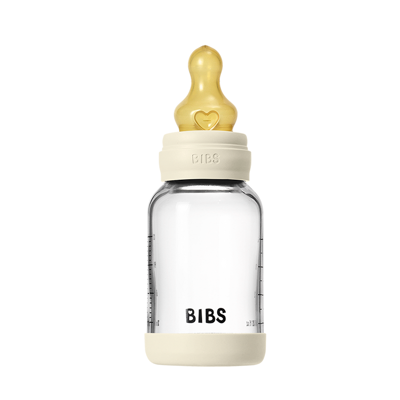 Clear baby bottle with beige cap and heart-shaped nipple on a white background