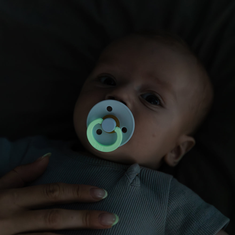 Baby with a glowing pacifier in a dark setting