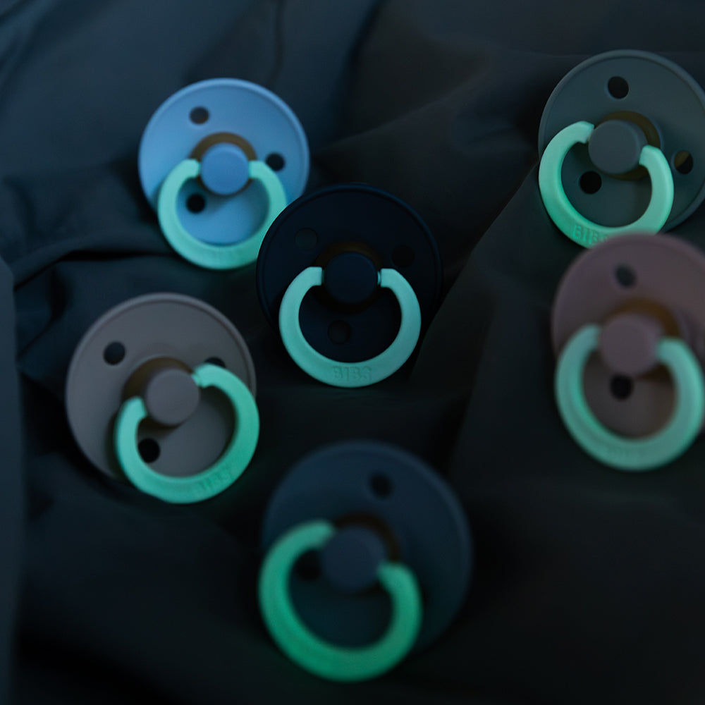 Multiple pacifiers with green rings on a dark background