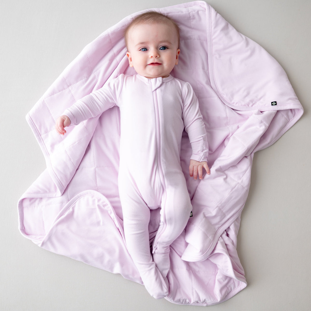 Baby in a white onesie lying on a pink blanket against a light gray background