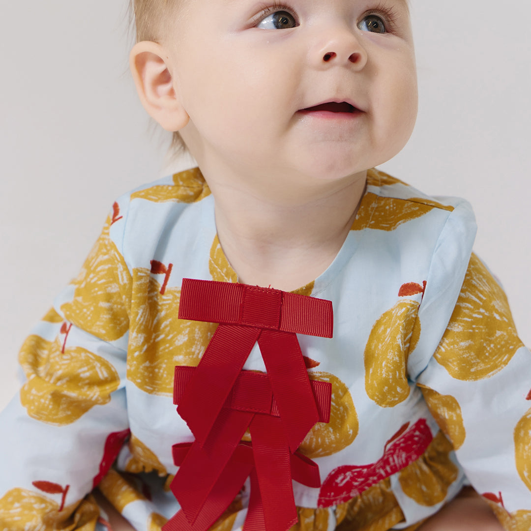 Baby wearing a bib with yellow fruit pattern and a red bow