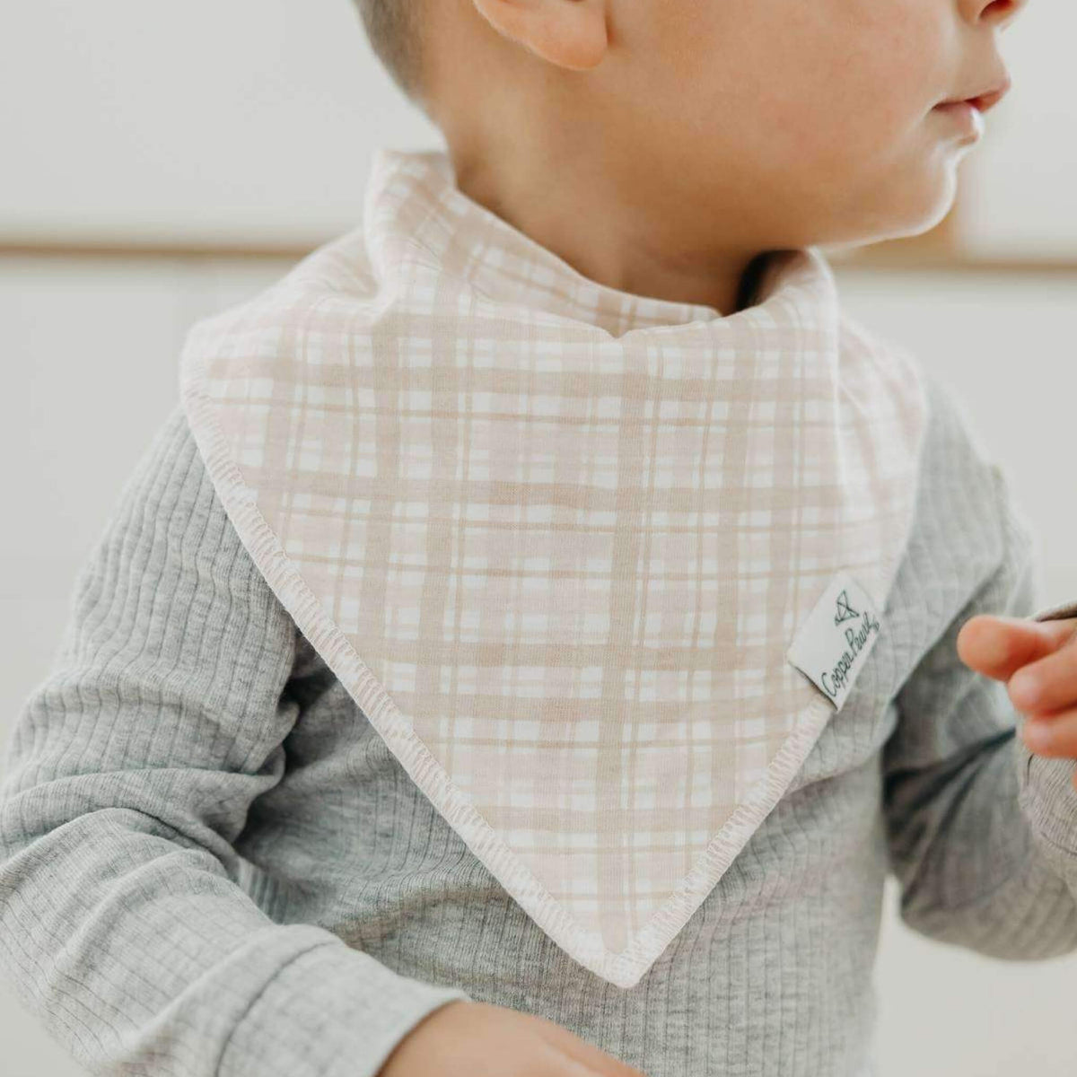 Child wearing a checkered bib with a brand tag, against a neutral background