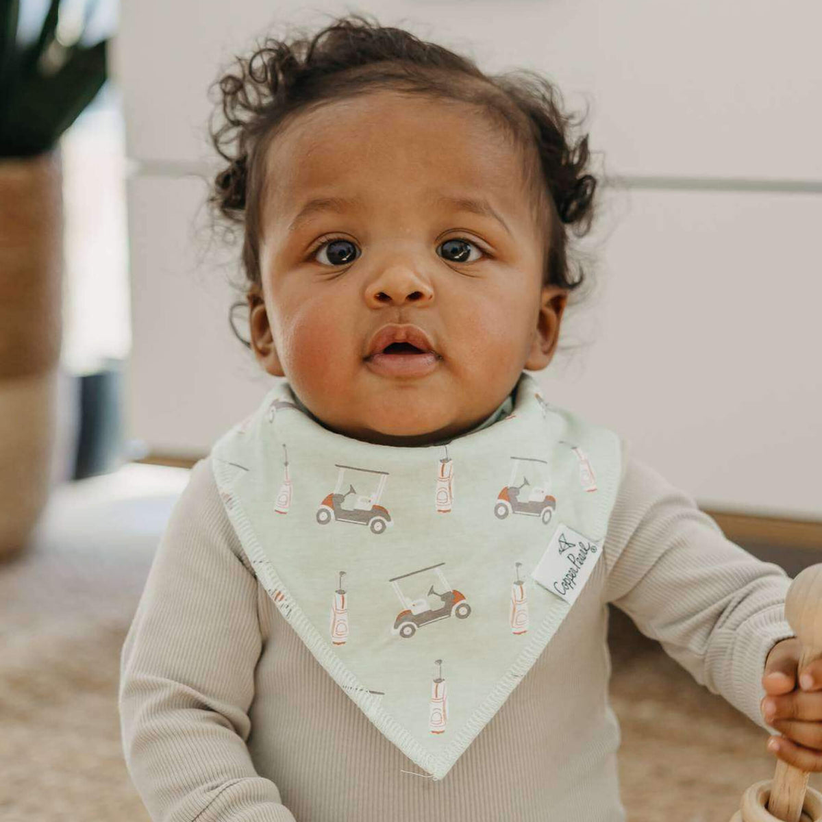 Baby wearing a light green bib with car patterns indoors