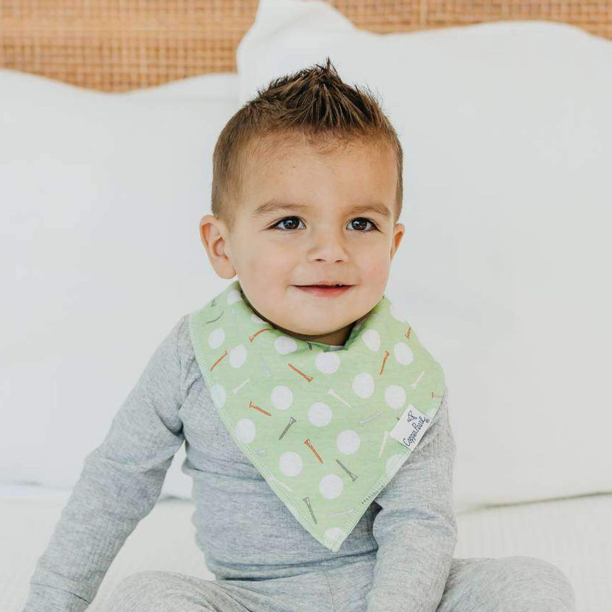 Child wearing a green bib with white polka dots and brown arrows, sitting on a white couch.