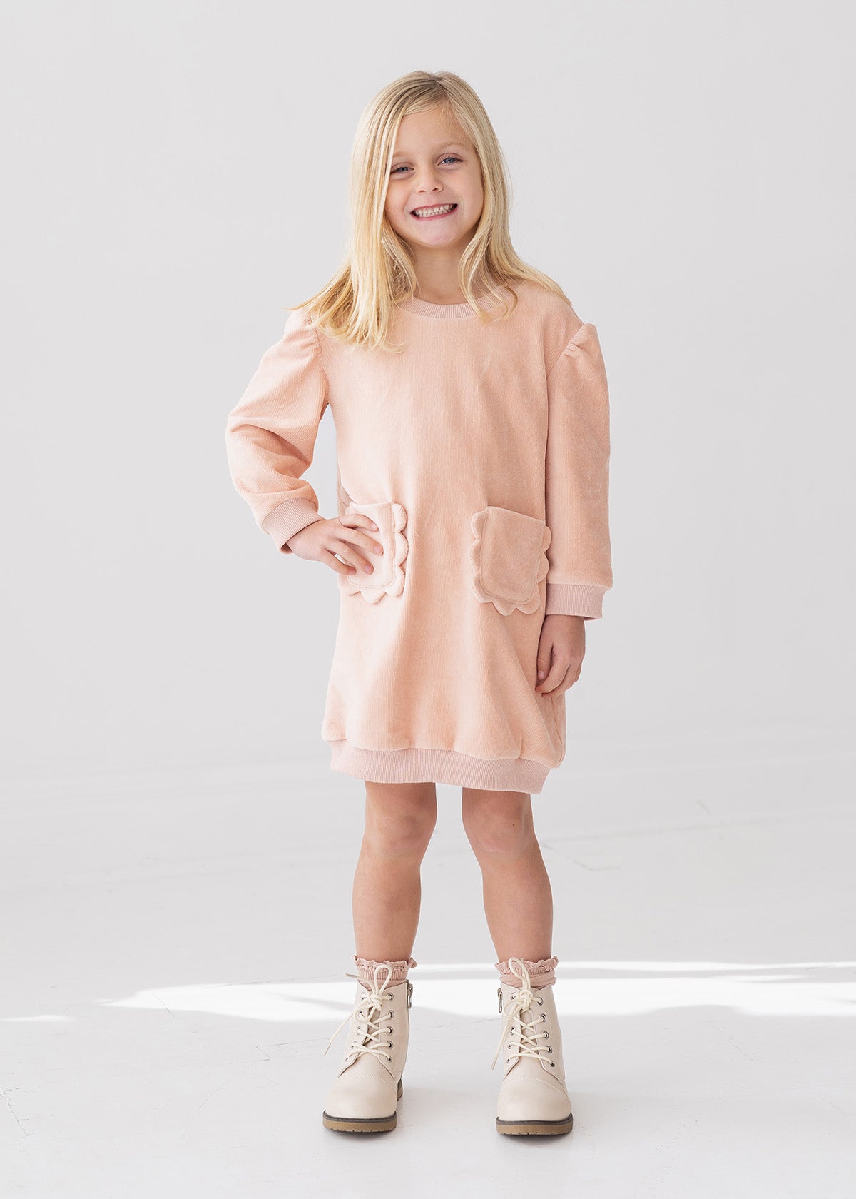 Young girl wearing a pink dress with pocket details on a white background