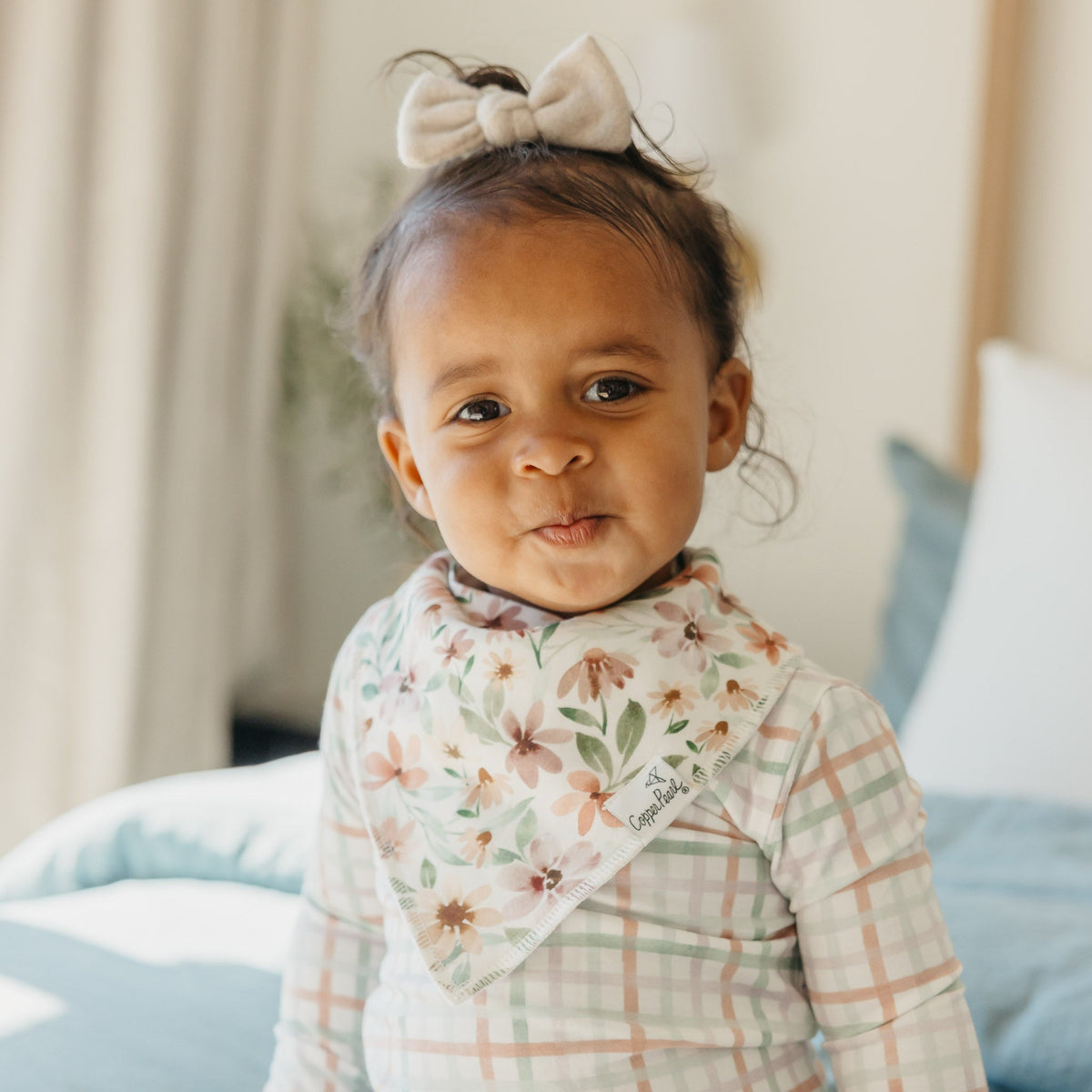 Young child wearing a floral and plaid outfit with a bow in their hair, sitting on a couch.