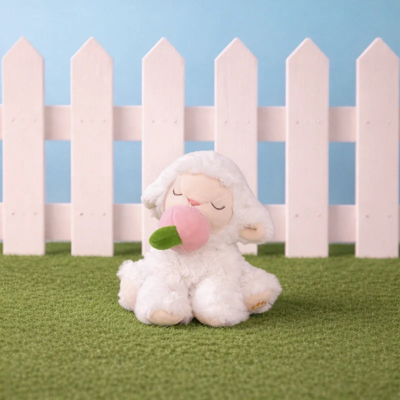 Plush lamb toy with a pink bubble gum sitting on grass in front of a white picket fence.