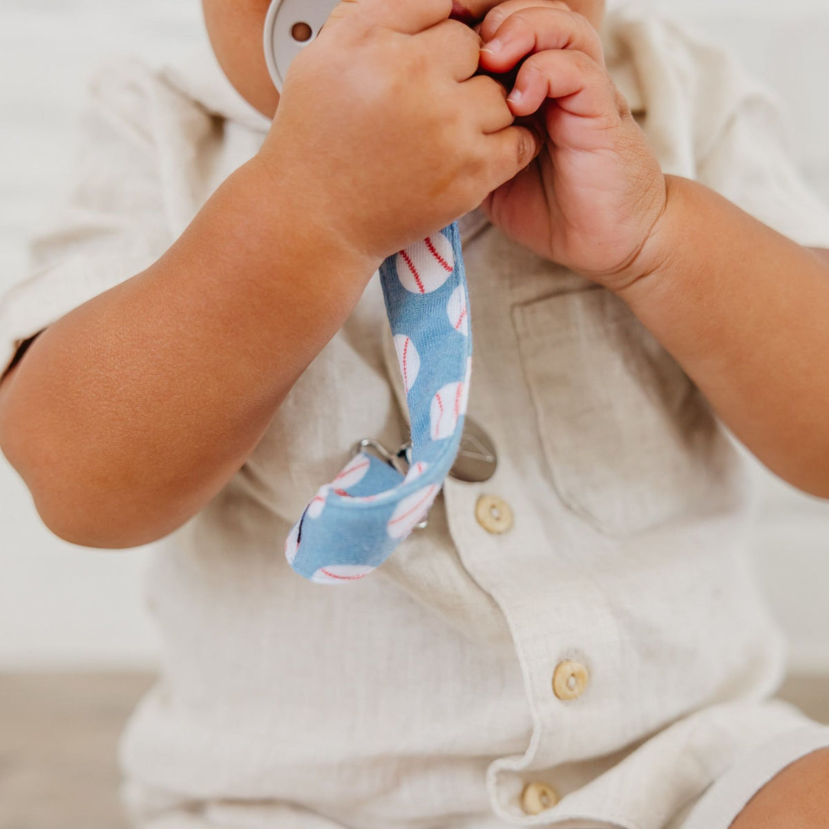 Close-up of a baby's hands holding a blue teething ring with pink patterns.