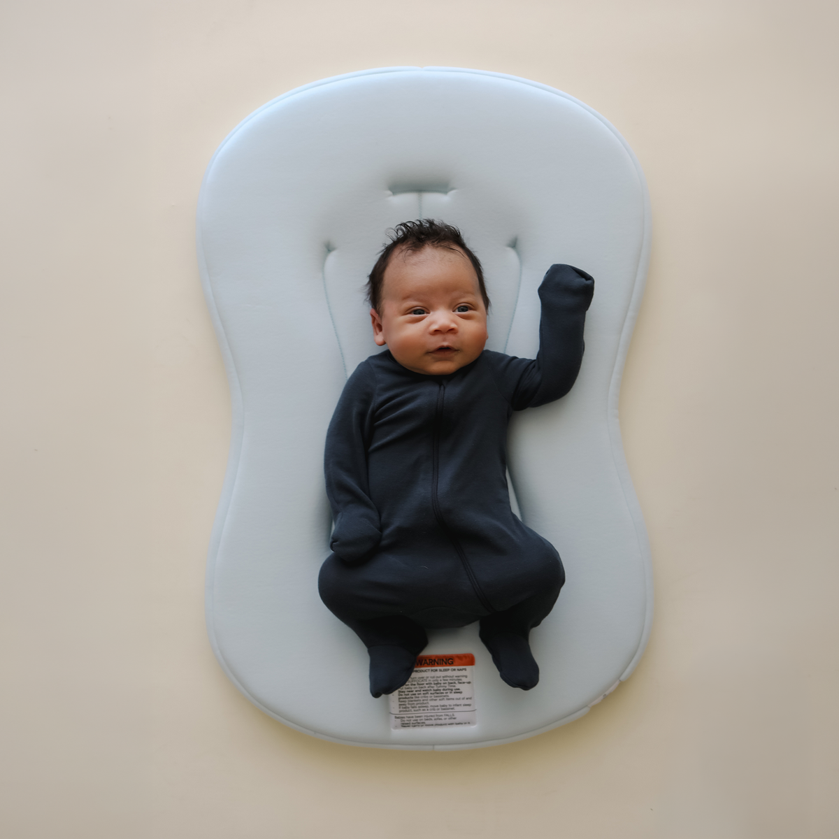 Newborn baby lying on a gray inflatable cushion against a beige background