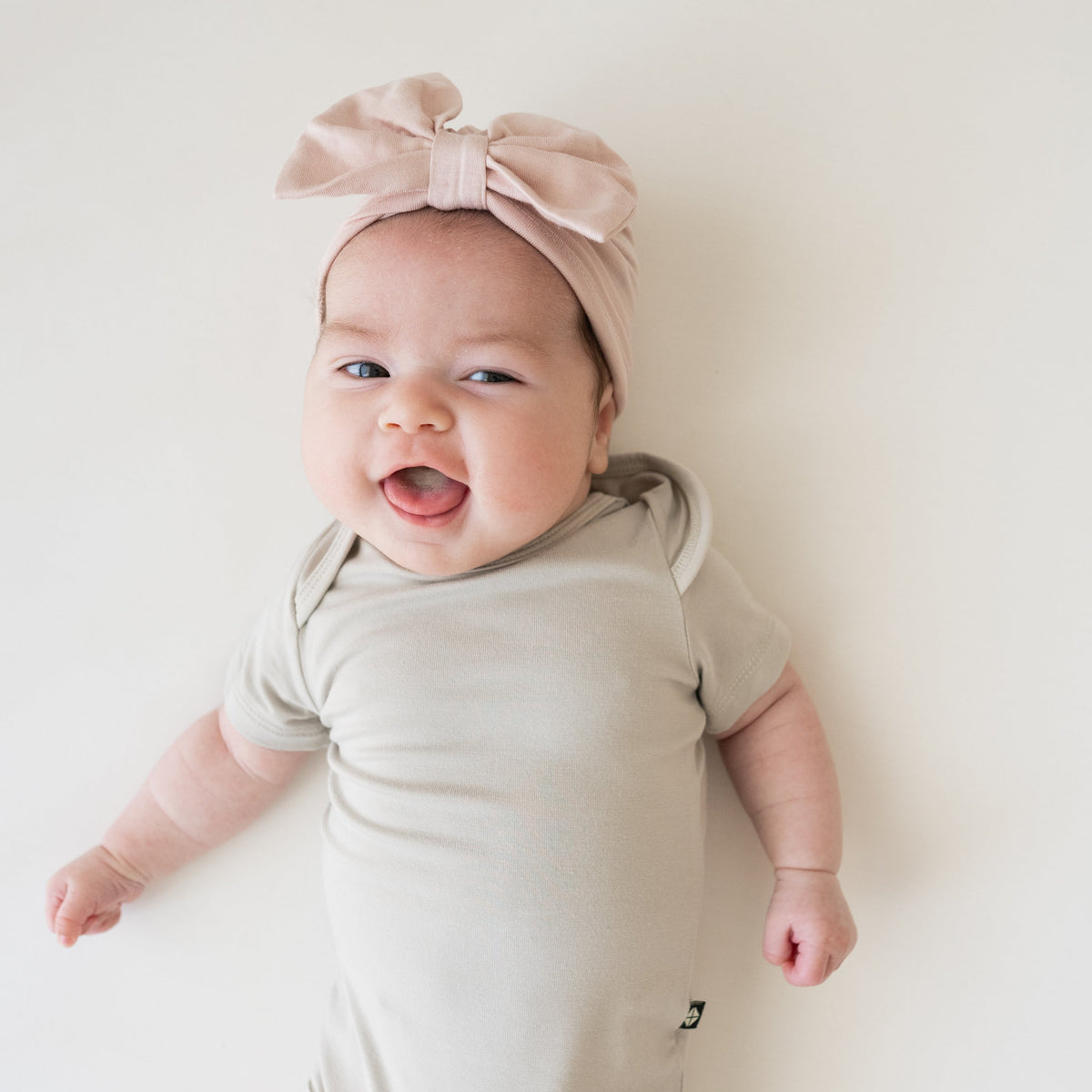 Baby wearing a light pink headband and beige onesie on a white background