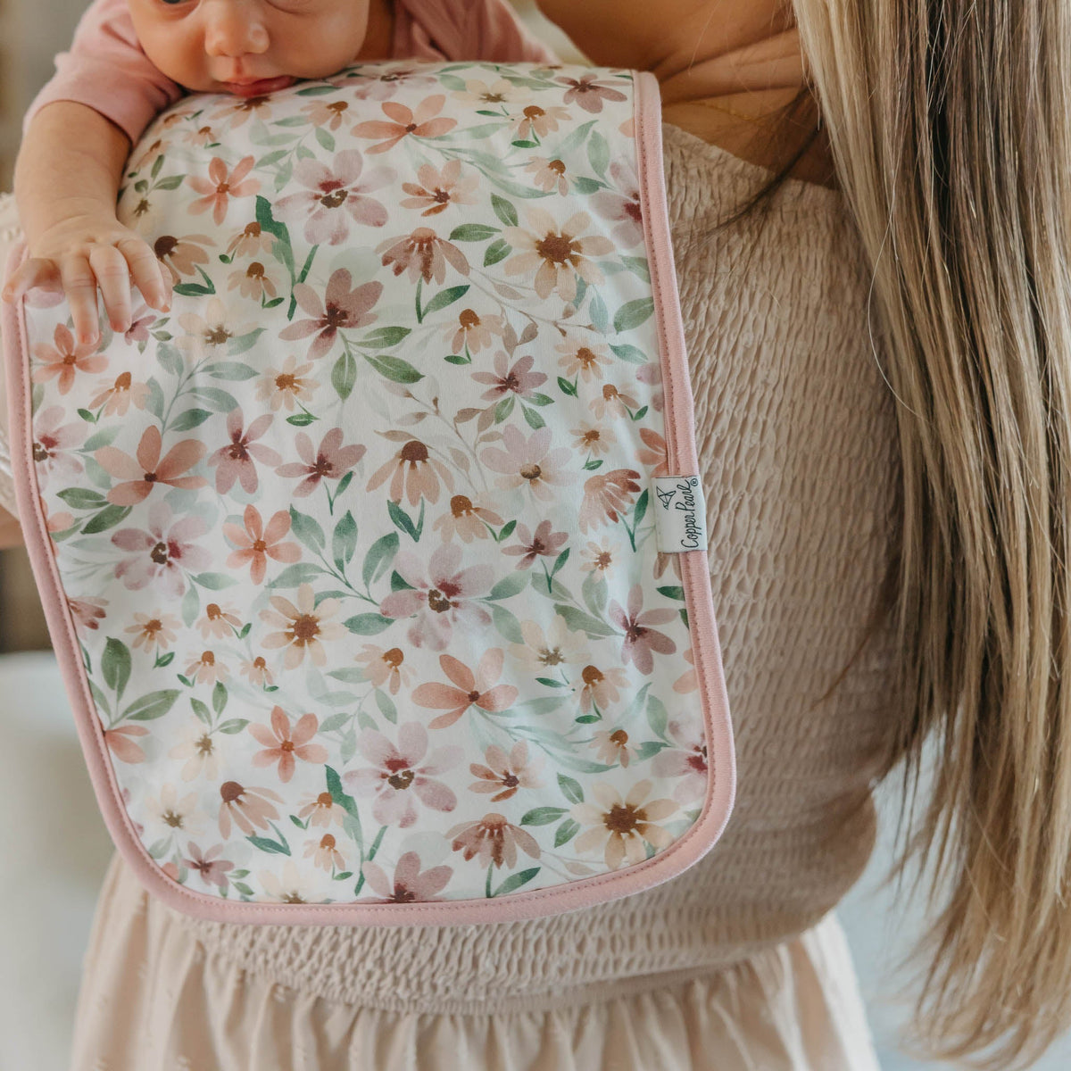Woman holding a baby wrapped in a floral blanket inside a home.