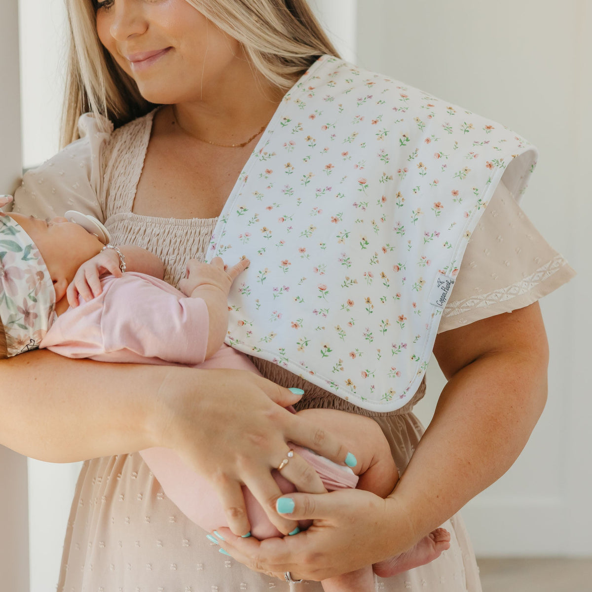 Woman holding a baby wrapped in a floral wrap with a neutral background