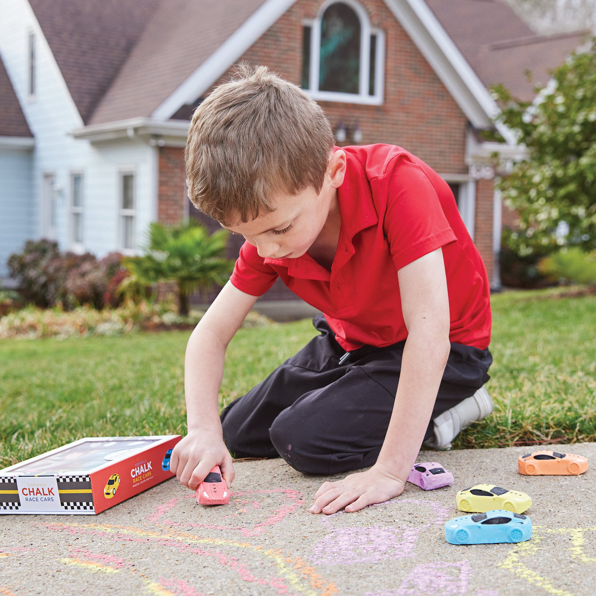 Child playing with toy cars on a driveway with a house in the background