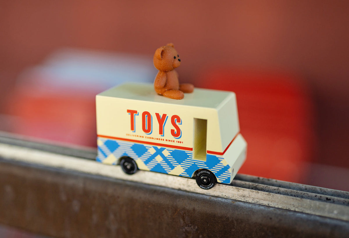 Toy truck with 'TOYS' on the side and a teddy bear on top, blurred background