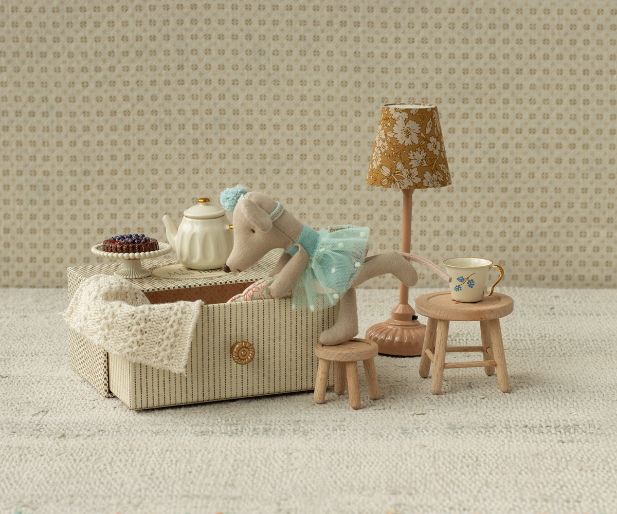Miniature tea set with teddy bear and lamp in a room with patterned wallpaper.