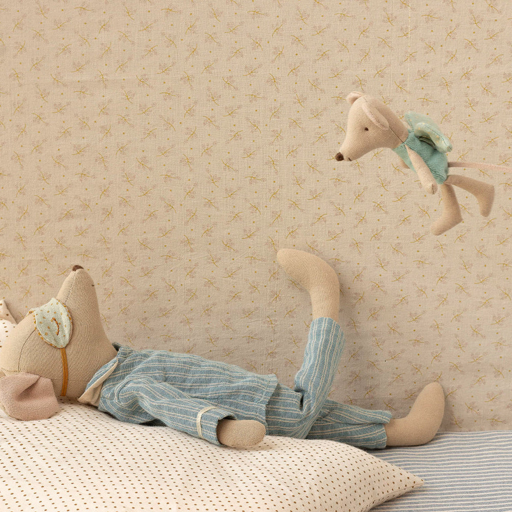 Stuffed animal toy lying on a bed with a decorative pillow against a patterned wall.