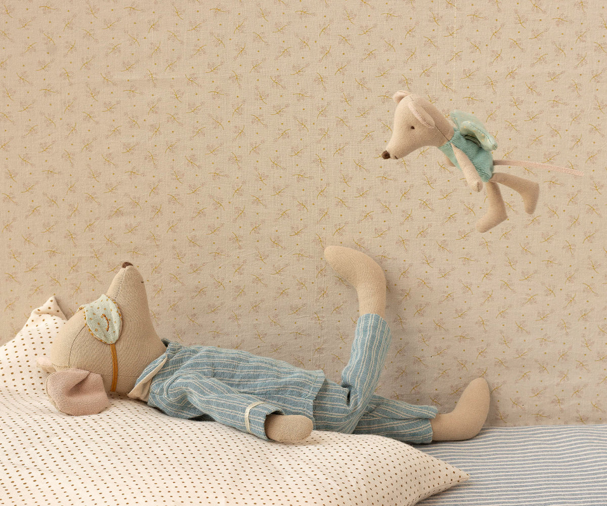 Stuffed animal toy lying on a bed with a decorative pillow against a patterned wall.