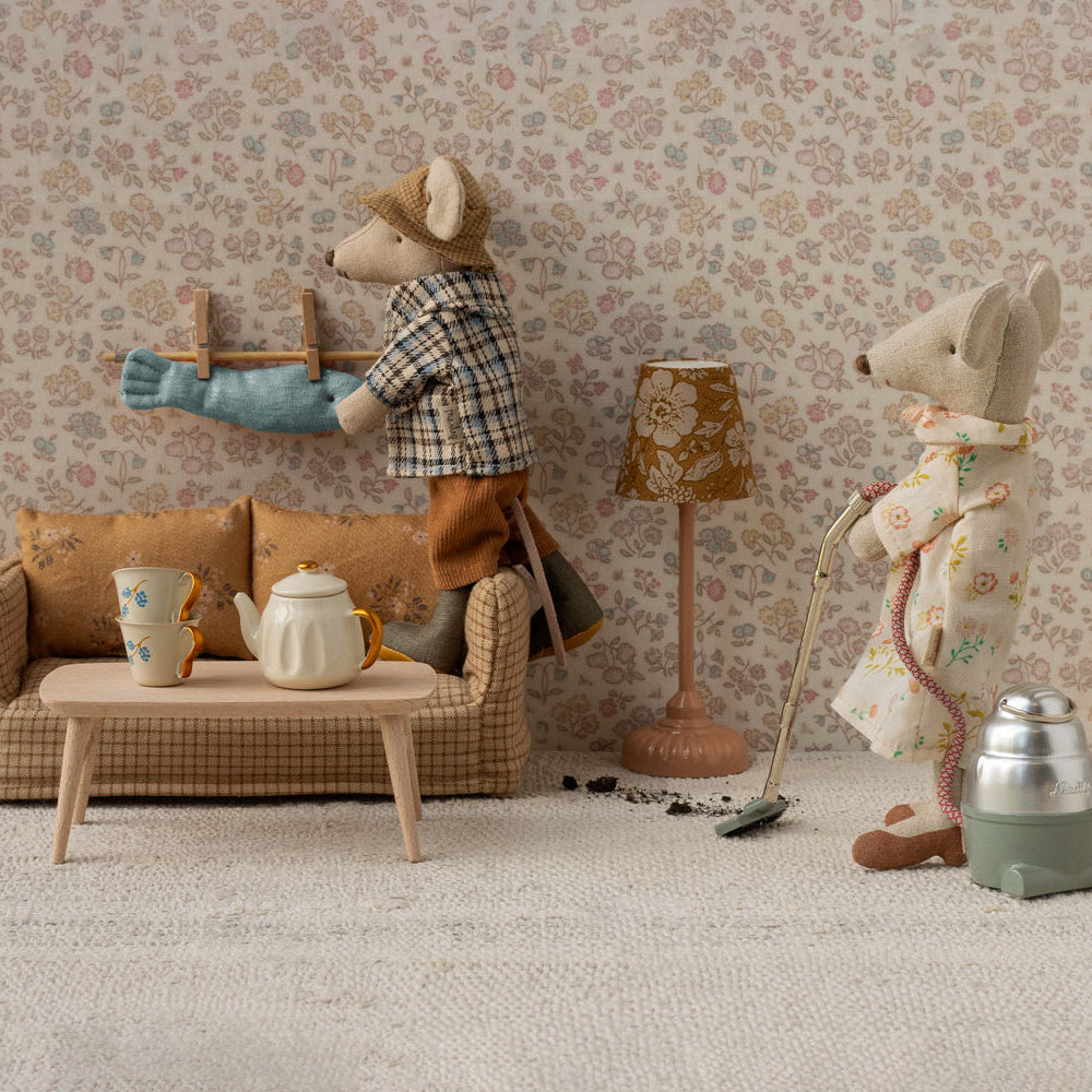 Miniature living room scene with toy mice and furniture against a floral wallpapered wall.