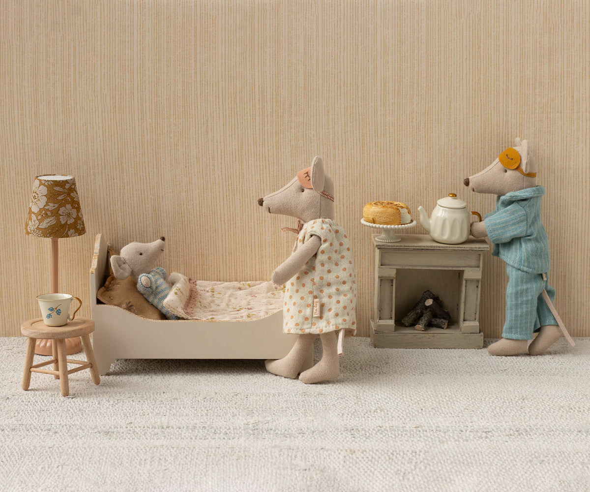 Miniature scene with toy mice in a room setting, including a bed, lamp, and small table.