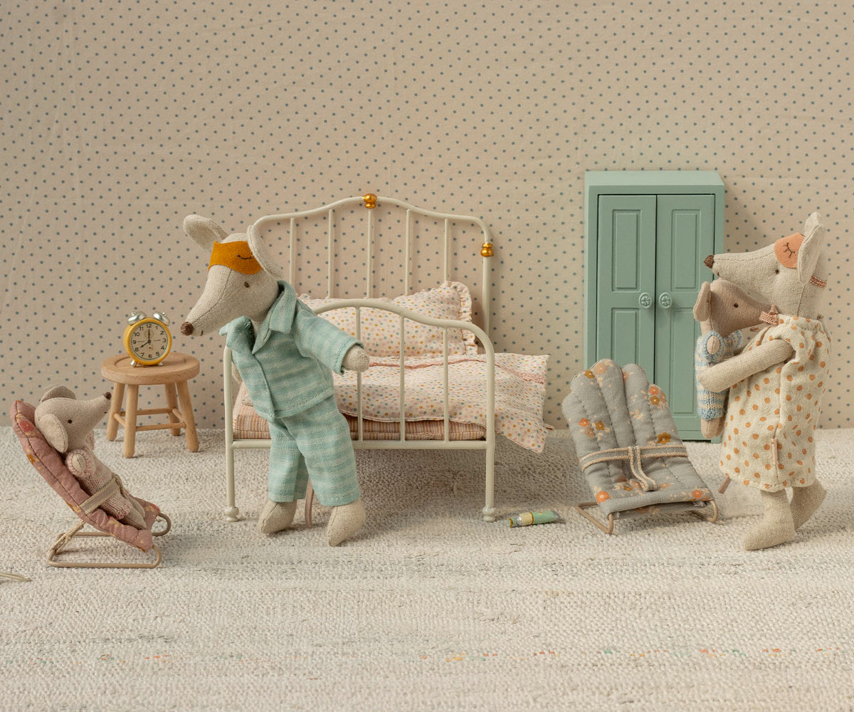 Miniature bedroom scene with toy mice and furniture against a patterned wall.