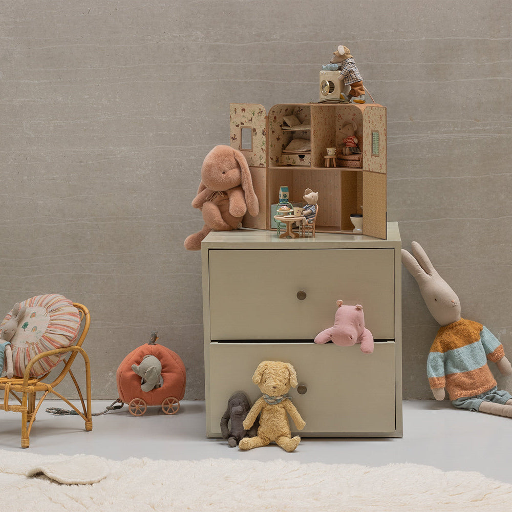Children's room with a dresser, toys, and a chair against a beige wall.
