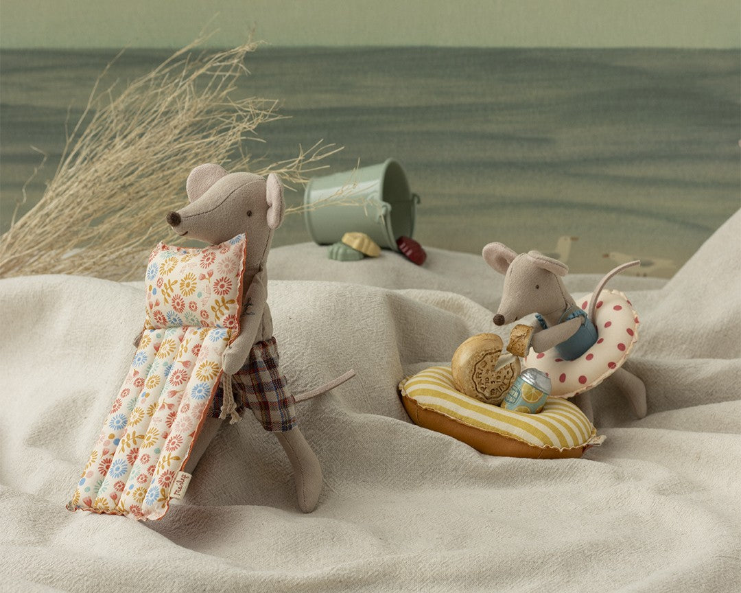 Two toy mice on a sandy beach with beach accessories