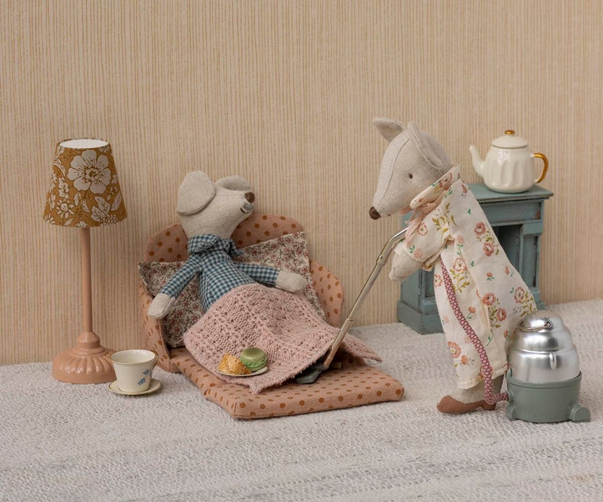 Two toy animals, a bear and a fox, in a cozy room setting with a lamp, table, and chair.